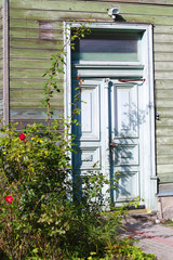 Fototapeta na wymiar old green wooden house with double doors and bush of red roses