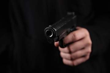 Gun in hand on black background. The threat of a firearm during a robbery on a dark street. Assault with a semiautomatic weapon.
