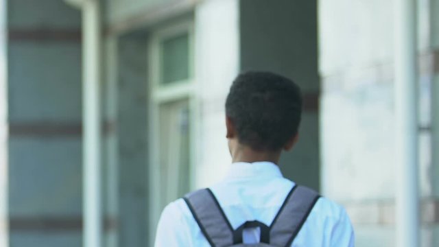 Student in uniform with rucksack walking to school building, academic year