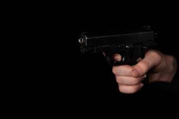 Gun in hand on black background. The threat of a firearm during a robbery on a dark street. Assault...