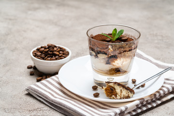 Portion of Classic tiramisu dessert in a glass cup on concrete background
