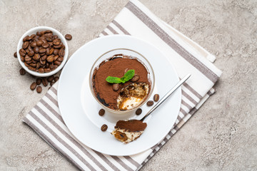 Portion of Classic tiramisu dessert in a glass cup on concrete background