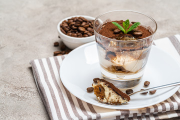 Portion of Classic tiramisu dessert in a glass cup on concrete background