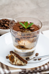 Portion of Classic tiramisu dessert in a glass cup on concrete background