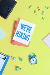 Obraz premium Text sign showing We Re Hiring. Business photo showcasing Advertising Employment Workforce Placement New Job Pile of empty papers with copy space on the table