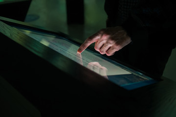 Man hand using interactive touchscreen display of electronic multimedia terminal at modern museum...