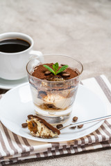 Portion of Classic tiramisu dessert in a glass and cup of coffee on concrete background