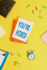 Text sign showing You Re Hired. Business photo showcasing New Job Employed Newbie Enlisted Accepted Recruited Pile of empty papers with copy space on the table