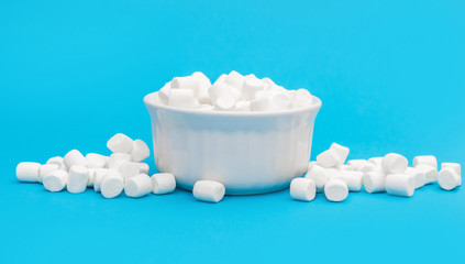 Heap of small marshmallow with full bowl of small marshmallow on blue.