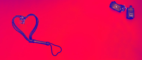 Accessories for bdsm on a red leather background. Lash in the shape of a heart and leather handcuffs. Valentine's Day. Erotic shop. Copy space, free space mockup