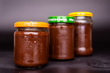 three jars of plum jam on a black background