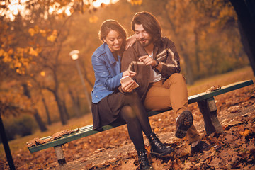 Young couple using cellphone in autumn colored park.