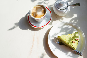 a piece of vegan, green matcha cake and a cup of coffee on a table in a restaurant, bright daylight makes beautiful shadows