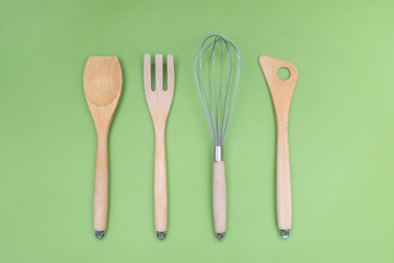 Wooden cooking utensils for kitchen. Spatulas, whisk and fork on green background. Natural design.