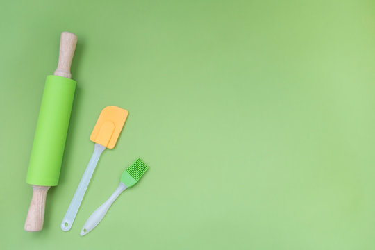 Kitchen silicone utensils for baking and cooking. Rolling pin, spatula and culinary brush on green background with copy space. Flat lay.