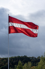 Latvian flag on the mast waving on the wind in the blue sky