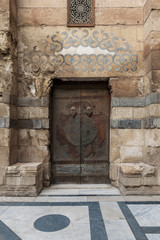 Stone bricks wall and wooden decorated copper plated door leading to Sultan Barquq mosque, Al-Moez Street, Old Cairo, Egypt