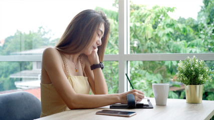 Young beautiful Asian woman enjoying a relaxing moment working and using mobile phone as mobile smart payment to pay for a coffee in the coffeeshop on a bright sunny day