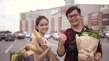 Happy cheerful vietnamese people standing with food bags on the background of big store and showing ok