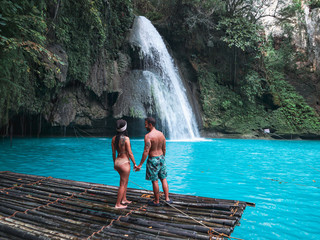 travel couple alone on the bamboo raft in front of the waterfall with turquoise water in Kawasan...