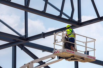 Professional installation work on a construction building site. Assemblers perform high-altitude installation works on the telescopic  boom lifts platforms. Installation of huge steel beams.