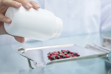 Chemist technician with class dispensing medicine pill on counter with laptop, beautiful Asian pharmacist standing in drugstore doing her work, pharmacist pay attention to the bottle of medicine