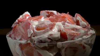 Fresh piece strawberries covered with thick layer of cream in glassware on black background. Camera rotation 360 degrees, close-up. 4K - 50fps  