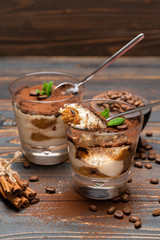 Portion of Classic tiramisu dessert in a glass and savoiardi cookies on wooden background