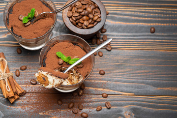 Portion of Classic tiramisu dessert in a glass and savoiardi cookies on wooden background