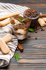 Portion of Classic tiramisu dessert in a glass and savoiardi cookies on wooden background