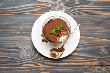 Portion of Classic tiramisu dessert in a glass cup on wooden background