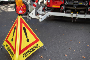 Dreieck, das Feuerwehr bei der Arbeit zeigt. Deutsches Zeichen, Feuerwehrauto im Hintergrund