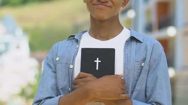 Happy teenage boy holding Bible, concept of religious vocation to clergy, priest