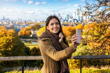 Portrait of a beautiful woman taking selfie pictures with her mobile phone at a Park with view to...