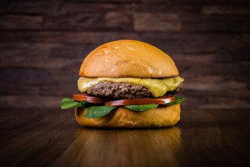 Craft beef burger with cheese and rocket leafs on wood table and rustic background.