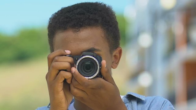 Teen boy taking picture with camera, smiling sincerely, value moments of life
