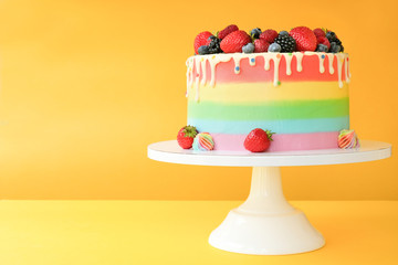 Cake on birthday with colorful rainbow cream on a yellow background decorated with berries,...