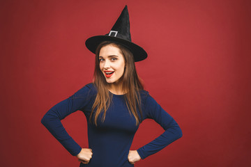 Halloween Party girl. Happy Halloween Witch with bright make-up and long hair. Beautiful young surprised woman posing in witches sexy costume. Isolated on red background.