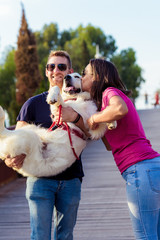 Beautiful romantic couple is having fun with their dog labrador retriever outdoors. Couple of guys playing with their dog on the park.Portrait of happy young couple hugging and kissing their dog