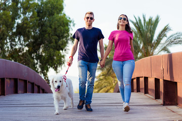 Romantic couple is on a walk in the city with their dog labrador. Beautiful young woman and handsome man are having fun outdoors with golden retriever labrador