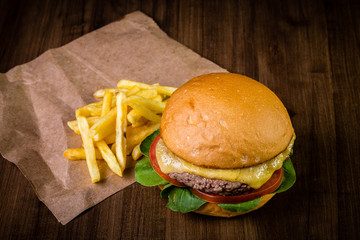 Craft beef burger with cheese, rocket leafs and french fries on wood table and rustic background.