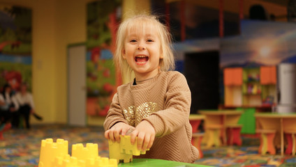 Cute little girl playing alone with colorful plastic educational toy blocks .