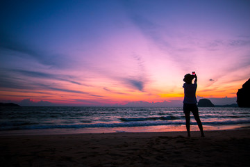 Silhouette of The girl is walking happily Use the phone at the beach during the sunset and her enjoying freedom feeling happy at sunset 