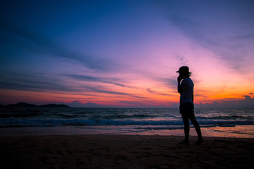 Fototapeta premium Silhouette of The girl is walking happily Use the phone at the beach during the sunset and her enjoying freedom feeling happy at sunset 