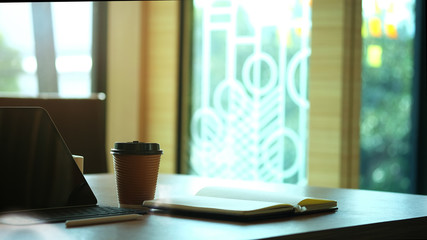 Paper cup of coffee on office workspace with morning light.