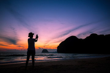 Fototapeta premium Silhouette of The girl is walking happily Use the phone at the beach during the sunset and her enjoying freedom feeling happy at sunset 