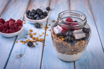 granola with yogurt and fresh berries in a glass on blue wooden background