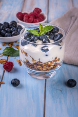 granola with yogurt and fresh berries in a glass on blue wooden background