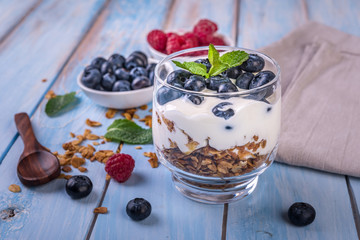 granola with yogurt and fresh berries in a glass on blue wooden background