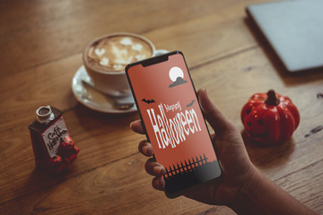 Happy Halloween Mobile phone mockup background concept. Hand Holding mobile phone in coffee shop.